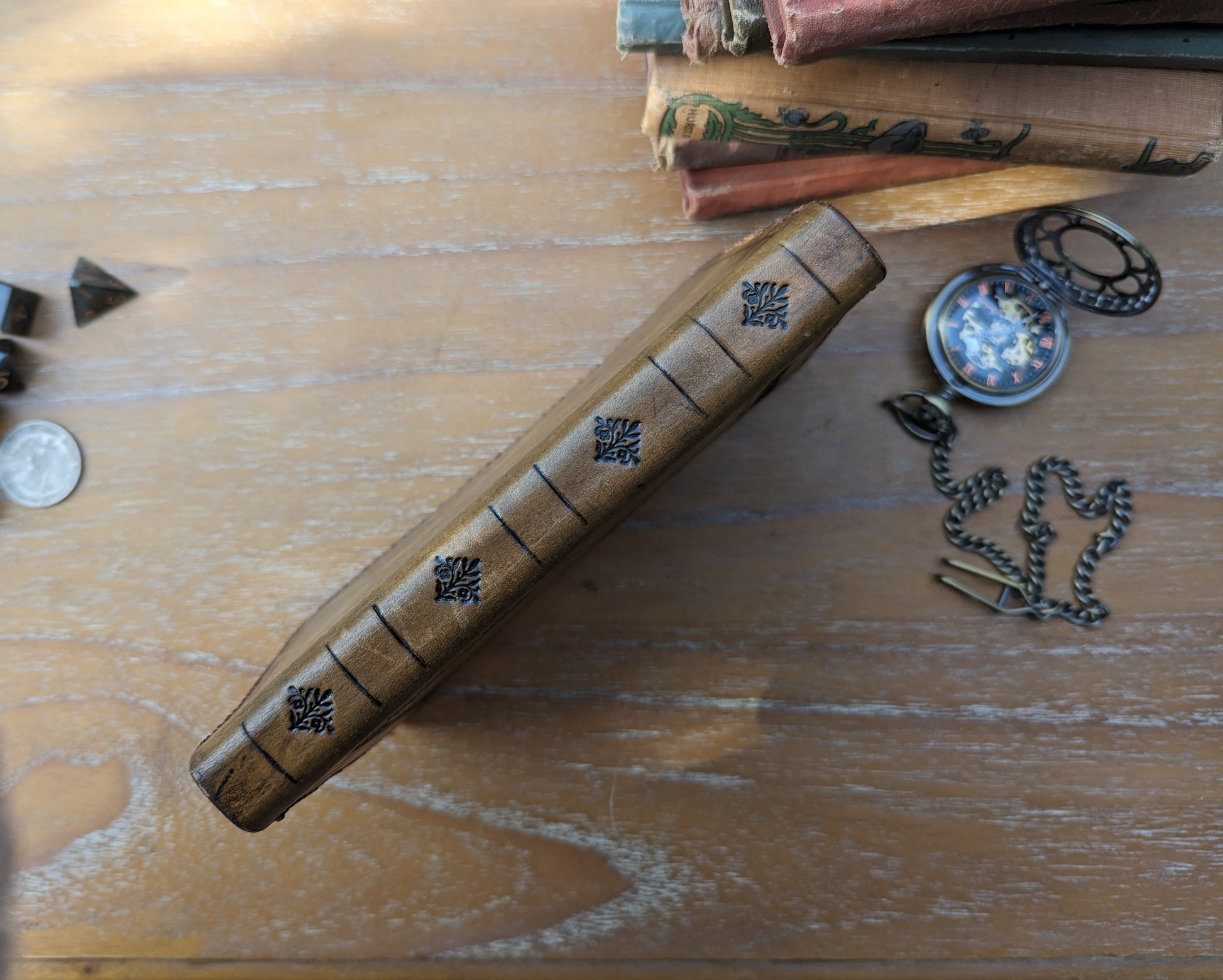 top down spine view of a dnd leather spellbook with a stack of books and a stopwatch