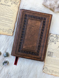 A handcrafted brown leather DnD spellbook with a dice and spell cards around it, presented on a white surface.