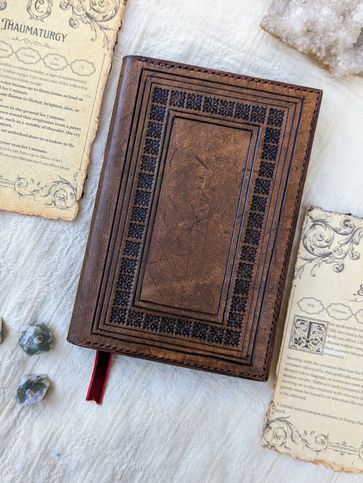 A handcrafted brown leather DnD spellbook with a dice and spell cards around it, presented on a white surface.