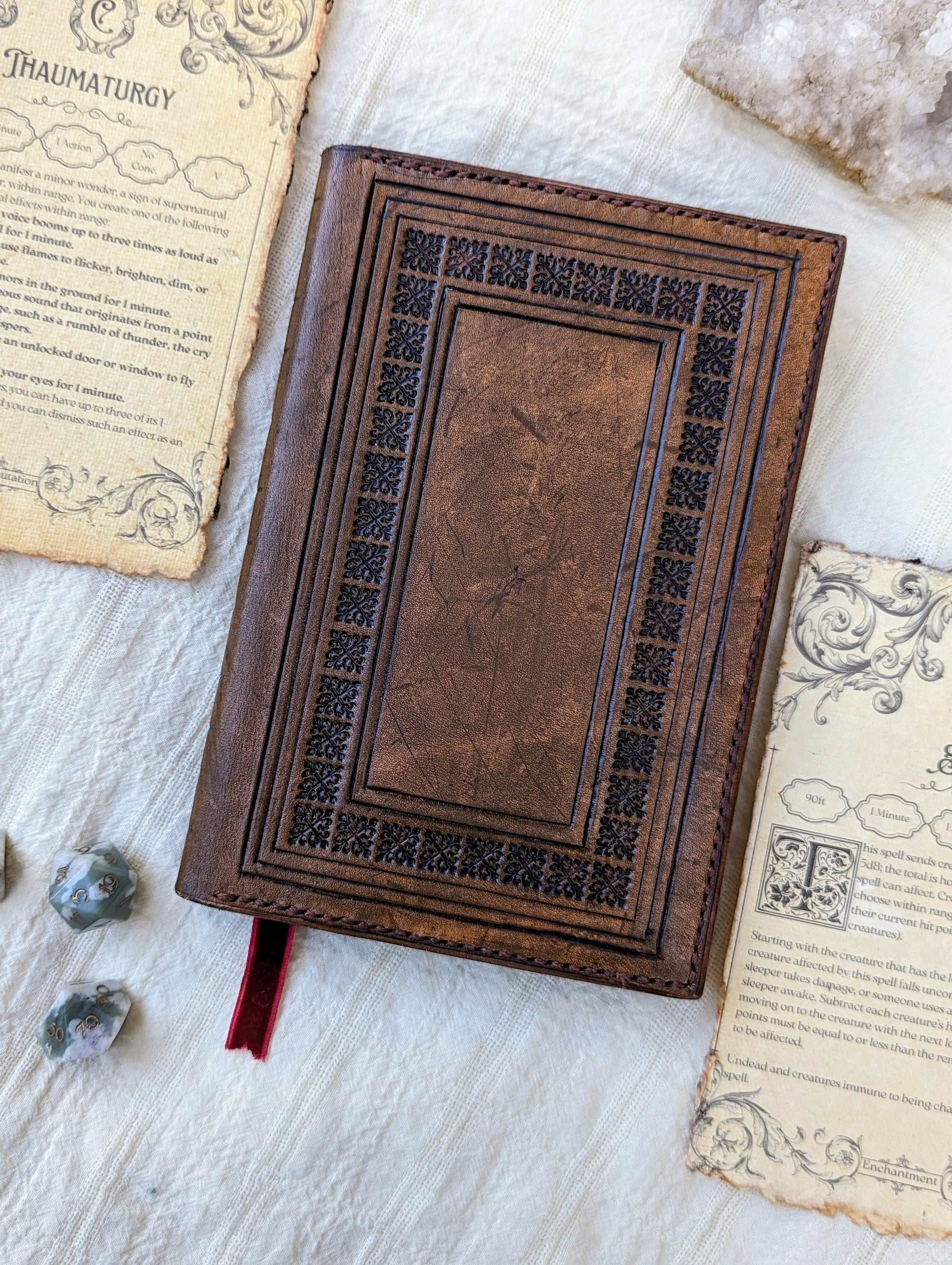 A handcrafted brown leather DnD spellbook with a dice and spell cards around it, presented on a white surface.