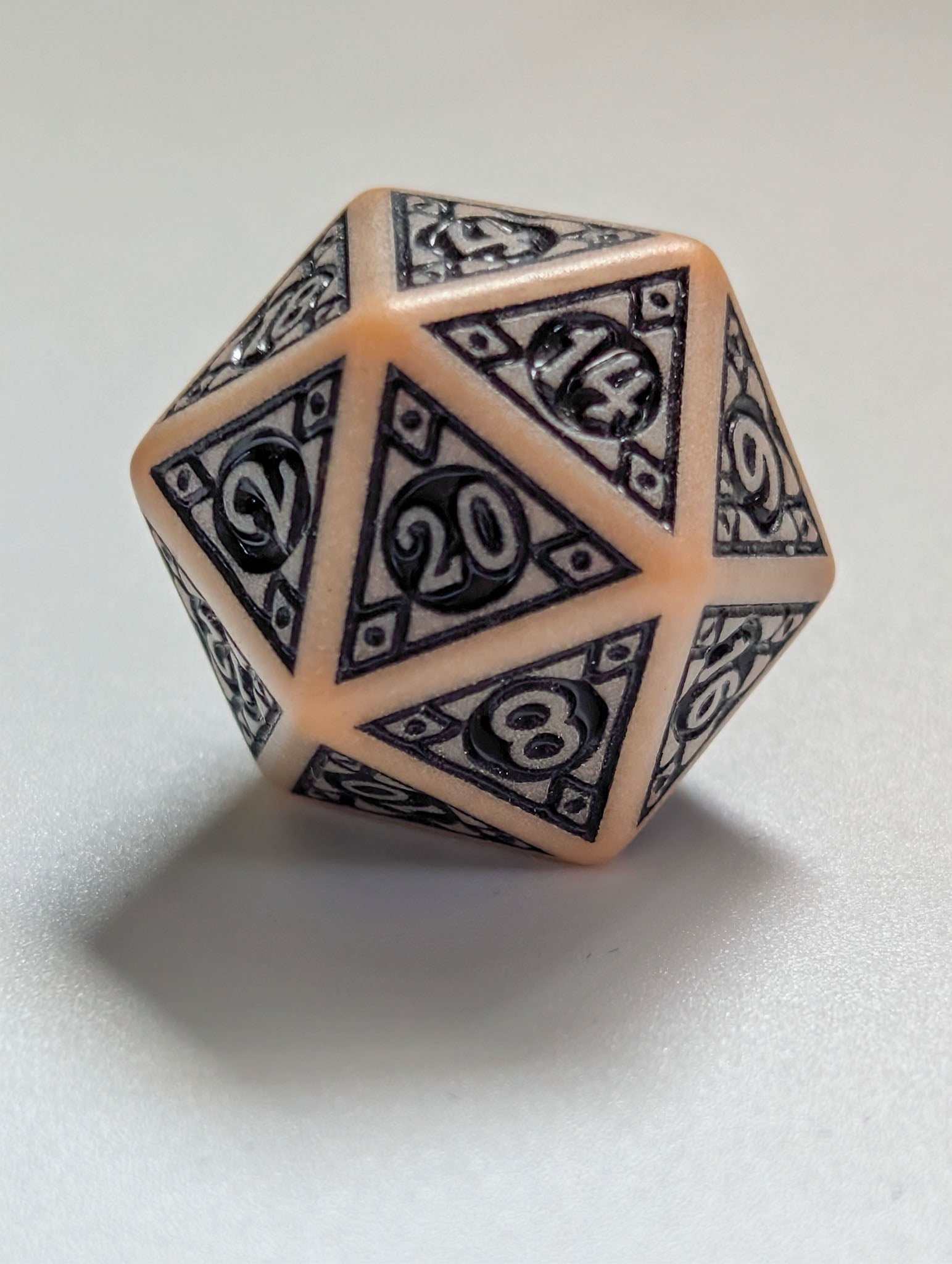 Close-up of The relic D20 with ornate black detailing and parchment-colored edges