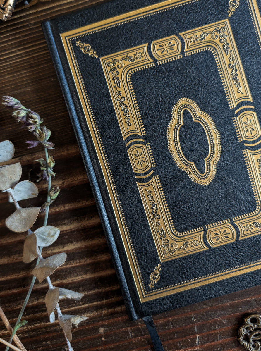 Black faux-leather Gothic D&D character journal with gold foil cover on a dark tabletop