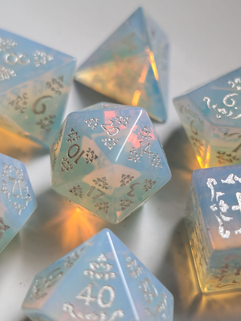 The Moonveil opalite polyhedral dice arranged together with pale blue and warm glowing tones