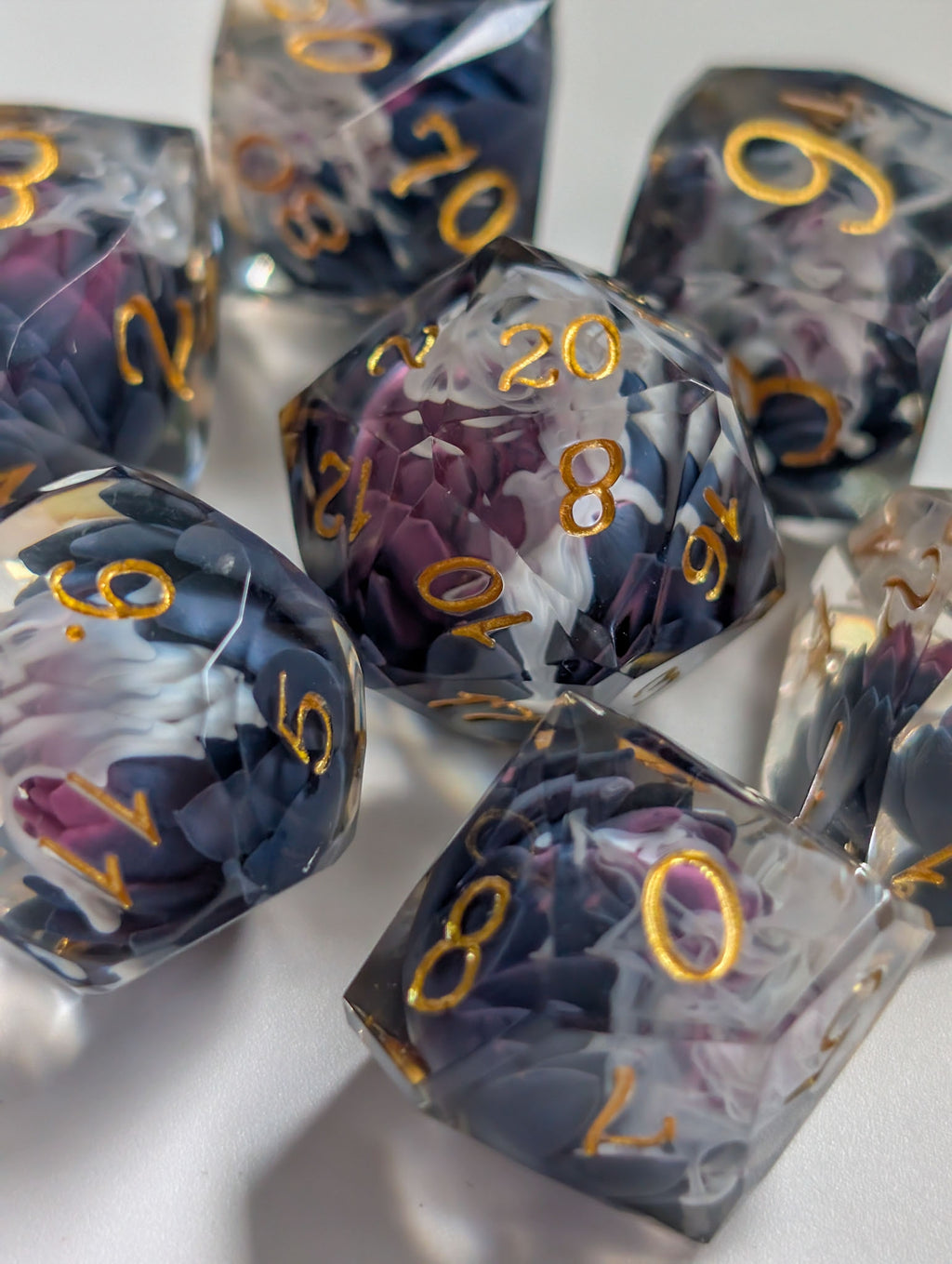 Close-up of The Nightbloom polyhedral dice showing dark purple floral inclusions and gold numbers